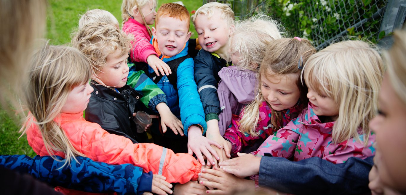 Børn i ring lægger deres hænder ovenpå hinanden Foto: Martin Gravgaard/TrygFondens Børneforskningscenter